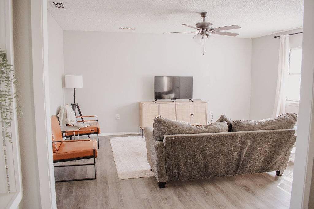 A living room with a sofa, a television on a cabinet, a ceiling fan, and a window with curtains.
