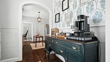 Une cuisine avec une machine à café ancienne, un meuble en bois doté de poignées en laiton et un papier peint à motifs.