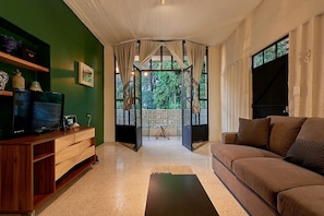 A living room with a wooden TV stand, a sofa, and a view through a glass door to an outdoor area. - La Mina AC Beauty Great Location Comfort (Oaxaca)