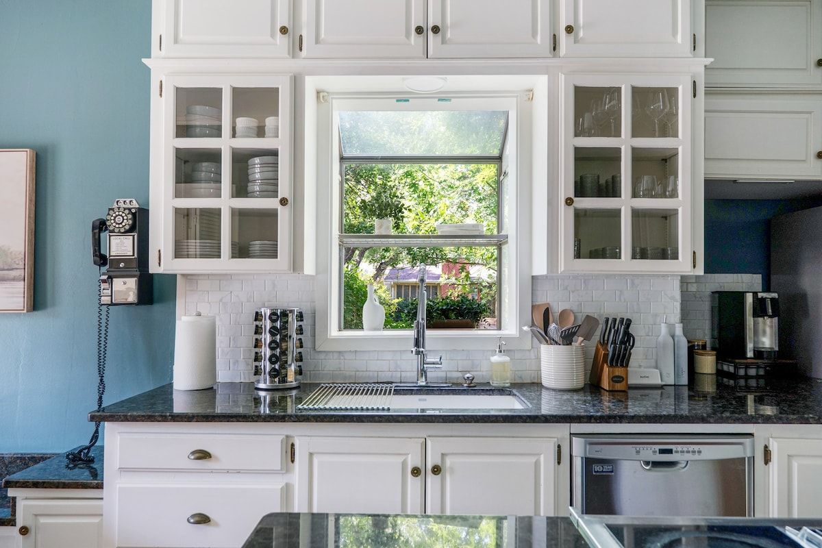 A kitchen with white cabinets, a window with a view of greenery, a sink, and a coffee maker.