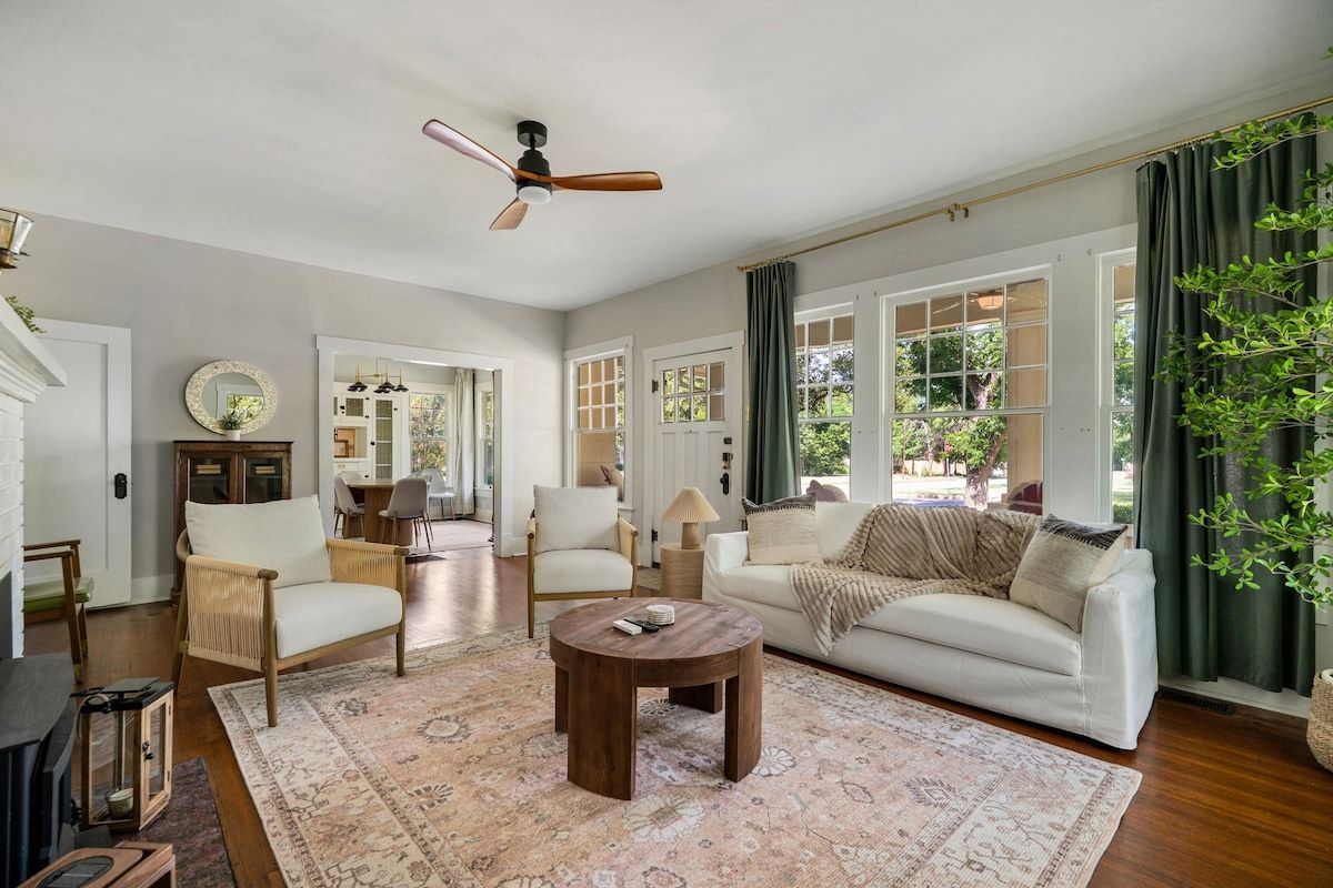 A spacious living room with a large window, a ceiling fan, and a wooden coffee table.