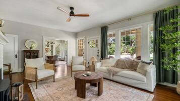 A spacious living room with a large window, a ceiling fan, and a wooden coffee table.