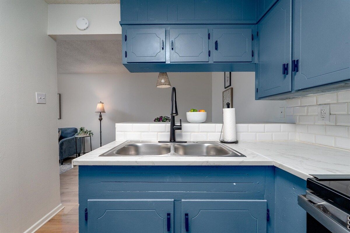 Une cuisine avec des meubles bleus, un plan de travail blanc et un robinet noir.