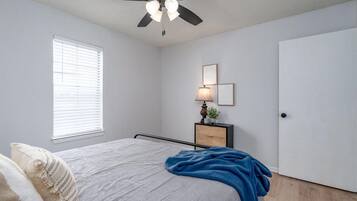 Ein Schlafzimmer mit einem Bett, einem Deckenventilator, einem Nachttisch mit Lampe und einer Tür.