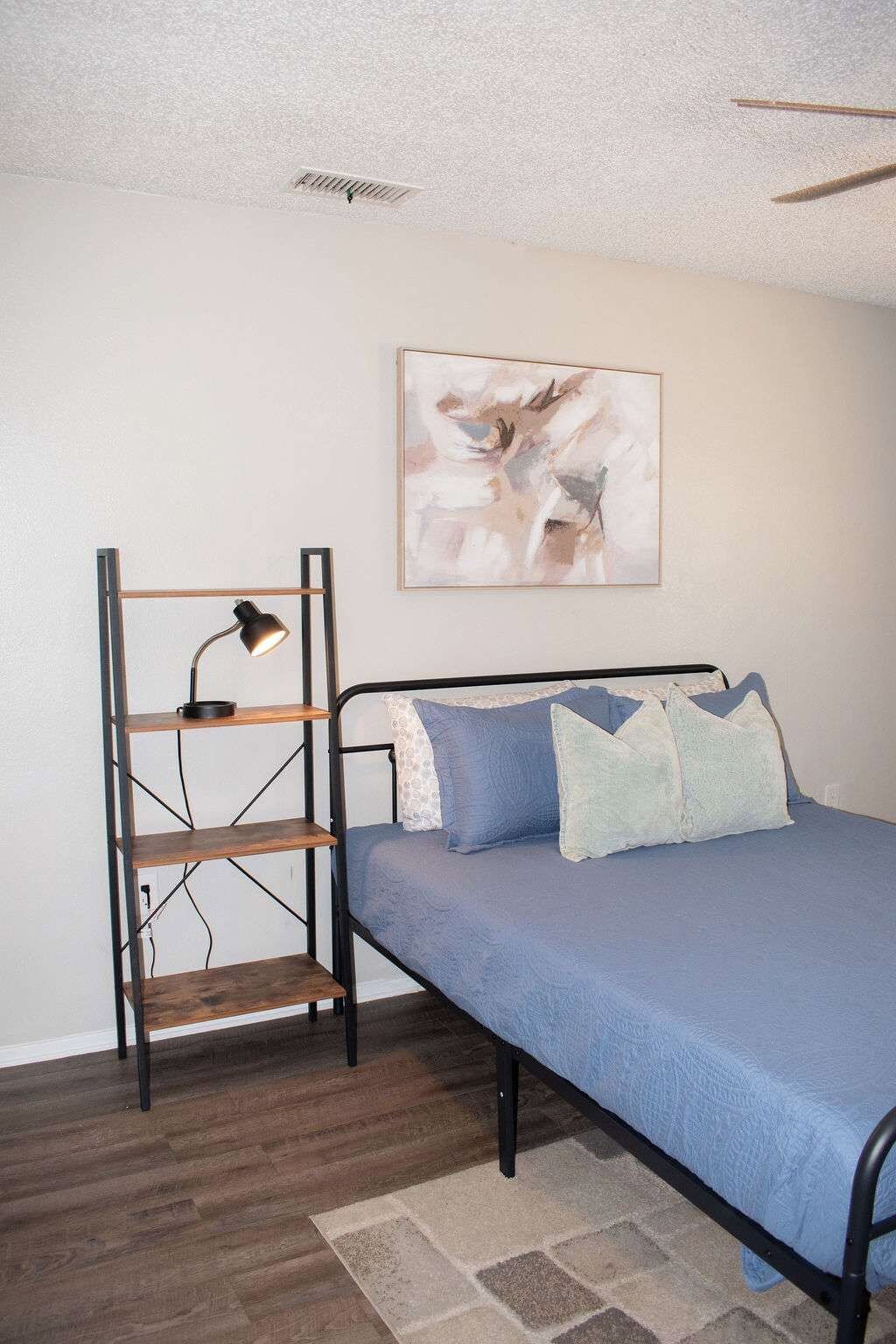 Une chambre à coucher avec un lit, une étagère fixée au mur, un ventilateur de plafond et un tableau.