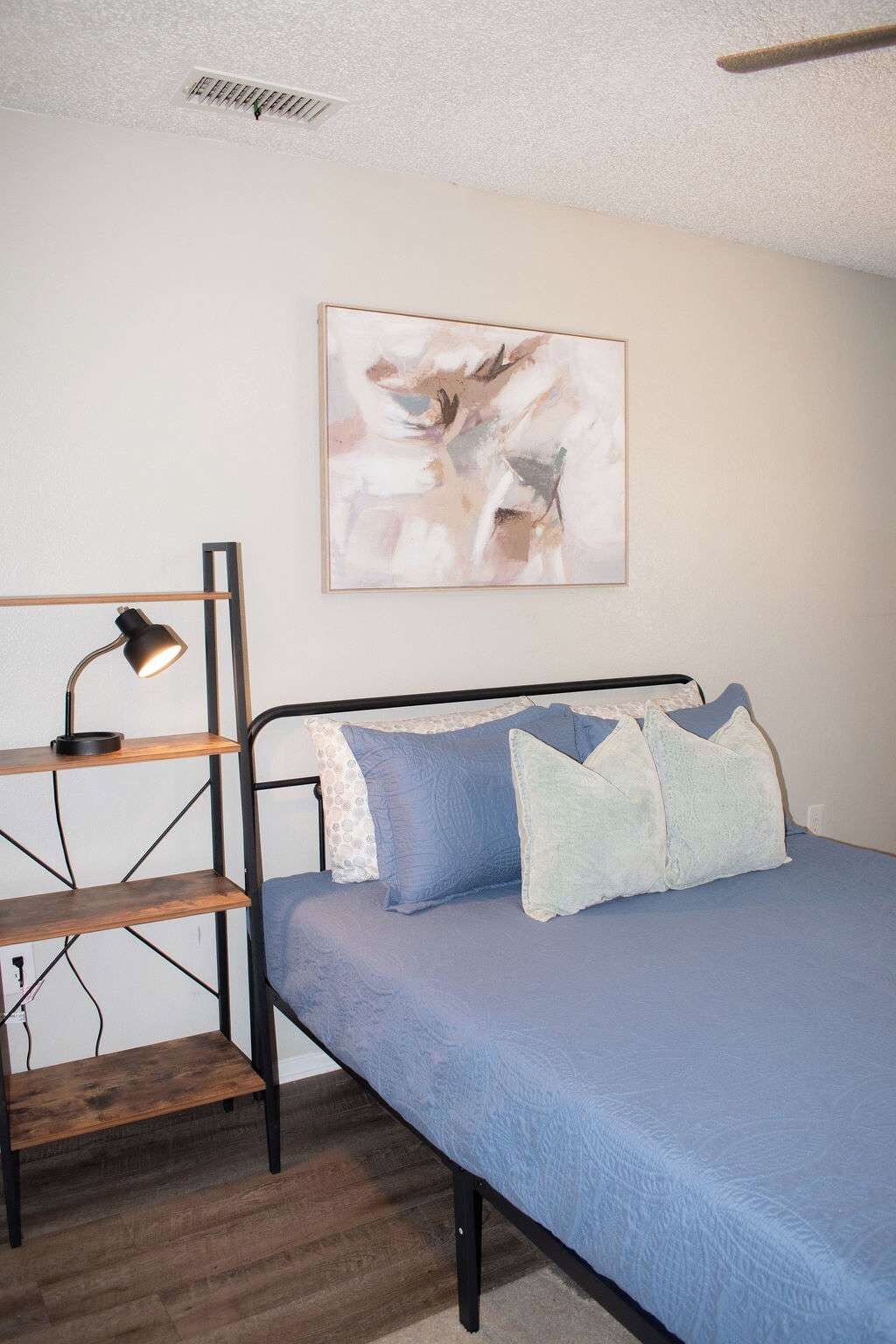 Un dormitorio con una cama, un escritorio con una lámpara y un cuadro en la pared.