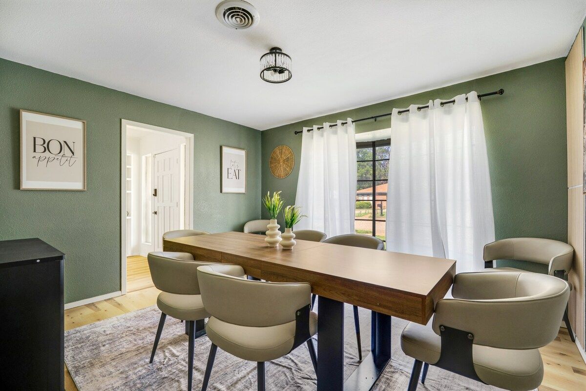 A dining area with a wooden table, six chairs, a rug, and a wall with framed artwork.