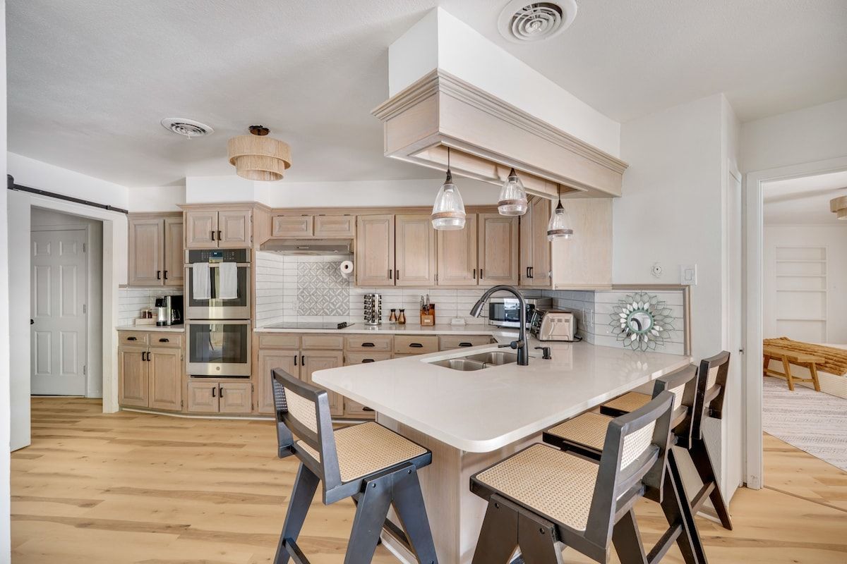 Een moderne keuken met houten kastjes, een centraal kookeiland met zitplaatsen, roestvrijstalen apparatuur en hanglampen.