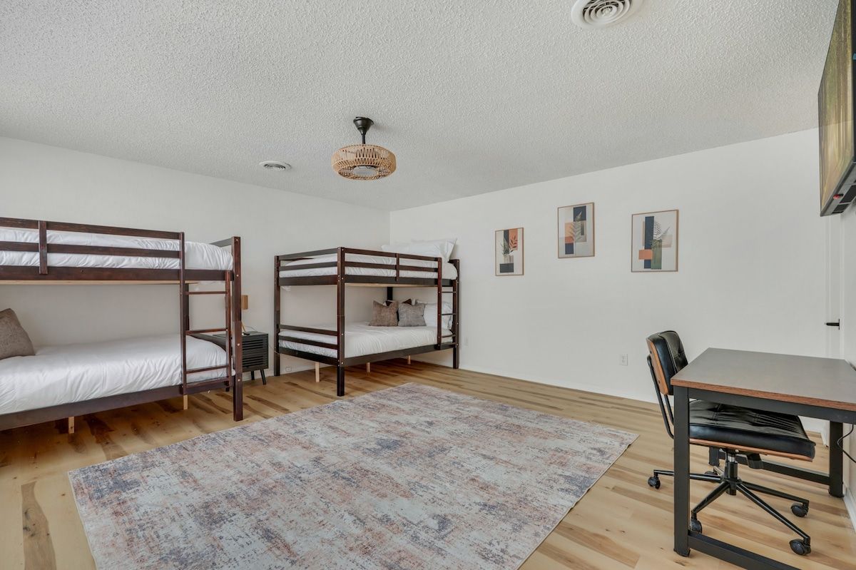 A room with bunk beds, a desk, a chair, and a patterned rug.