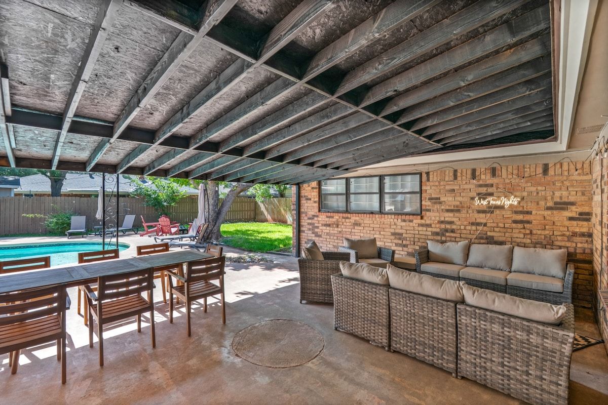 An outdoor patio with a pool, wooden furniture, and a brick wall.