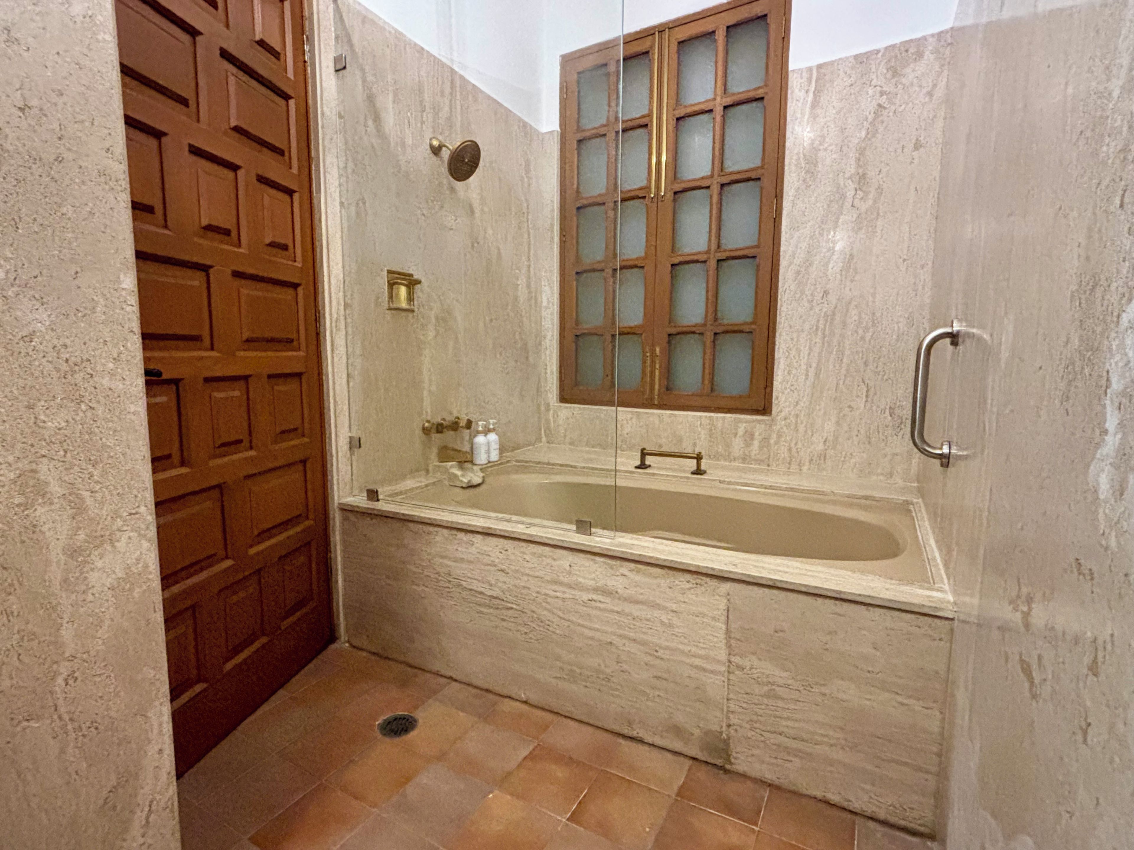 Une salle de bain avec une baignoire, une porte en bois, une fenêtre à vitres dépolies et une barre d’appui.