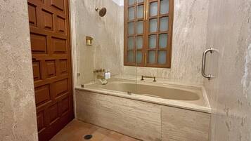 Une salle de bain avec une baignoire, une porte en bois, une fenêtre à vitres dépolies et une barre d’appui.