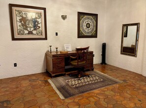 A room with a wooden desk, a chair, a patterned rug, and three framed artworks on the wall.