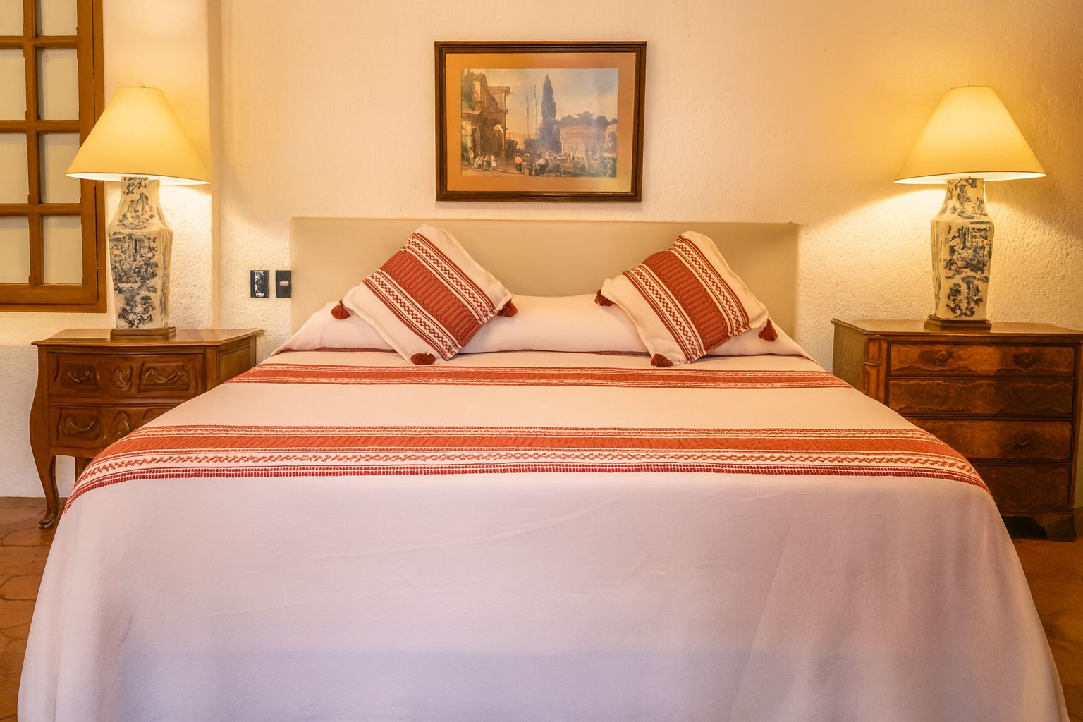 Une chambre d’hôtel avec un lit, deux tables de chevet, deux lampes et un tableau encadré au mur.