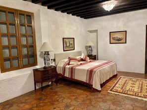 Une chambre à coucher avec une grande armoire en bois, un lit recouvert d’une couvre-lit à motifs, deux lampes de chevet et un tapis.