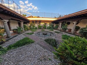 A courtyard with a central fountain, surrounded by stone pathways and greenery.