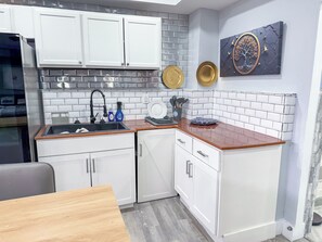 A compact kitchen with white cabinets, a wooden countertop, and a backsplash of white tiles. - The Pilot & Co-Pilot Suite (College Park)