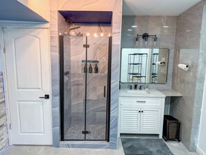 A bathroom with a glass-enclosed shower, a white vanity with a mirror, and a tiled floor. - The Pilot & Co-Pilot Suite (College Park)