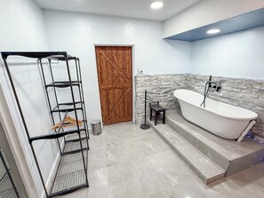 Ein Badezimmer mit einer Badewanne, einer Holztür und einem Metallregal.