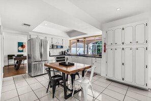 A modern kitchen with white cabinetry, a stainless steel refrigerator, a dining table with chairs, and a view of the outdoors through a large window. - Bayfront Villa 4 BR with Heated Pool 10 min walk to Beach (Hollywood)