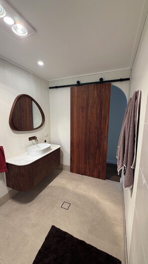 A bathroom with a wooden vanity, a large mirror, a white sink, and a towel rack. - Elevated Central getaway in Nowra (Nowra)