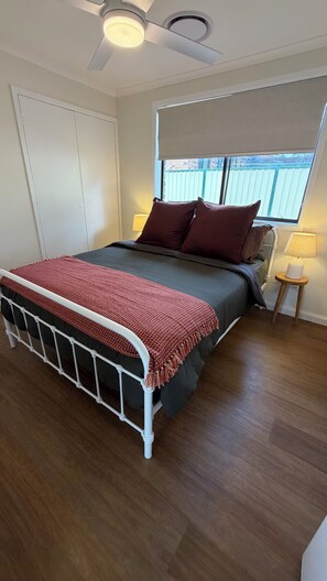 A bedroom with a bed, a ceiling fan, a window with a view, and a bedside table with a lamp. - Elevated Central getaway in Nowra (Nowra)