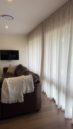 A living room with a brown sofa, a white throw blanket, and sheer curtains. - Elevated Central getaway in Nowra (Nowra)