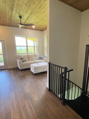 A spacious room with a wooden ceiling, a white sofa, and a black railing. - Secluded Hot Springs Cabin with Mountain Views & Fire Pit (Hot Springs)