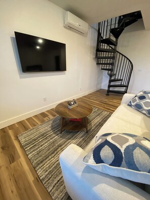 A modern living room with a flat-screen TV mounted on the wall, a wooden coffee table, a patterned sofa, and a spiral staircase. - Secluded Hot Springs Cabin with Mountain Views & Fire Pit (Hot Springs)