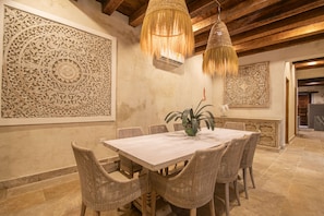 Un coin repas avec une table en bois et des chaises en osier, entouré de sculptures complexes sur les murs et agrémenté de lampes en osier suspendues.
