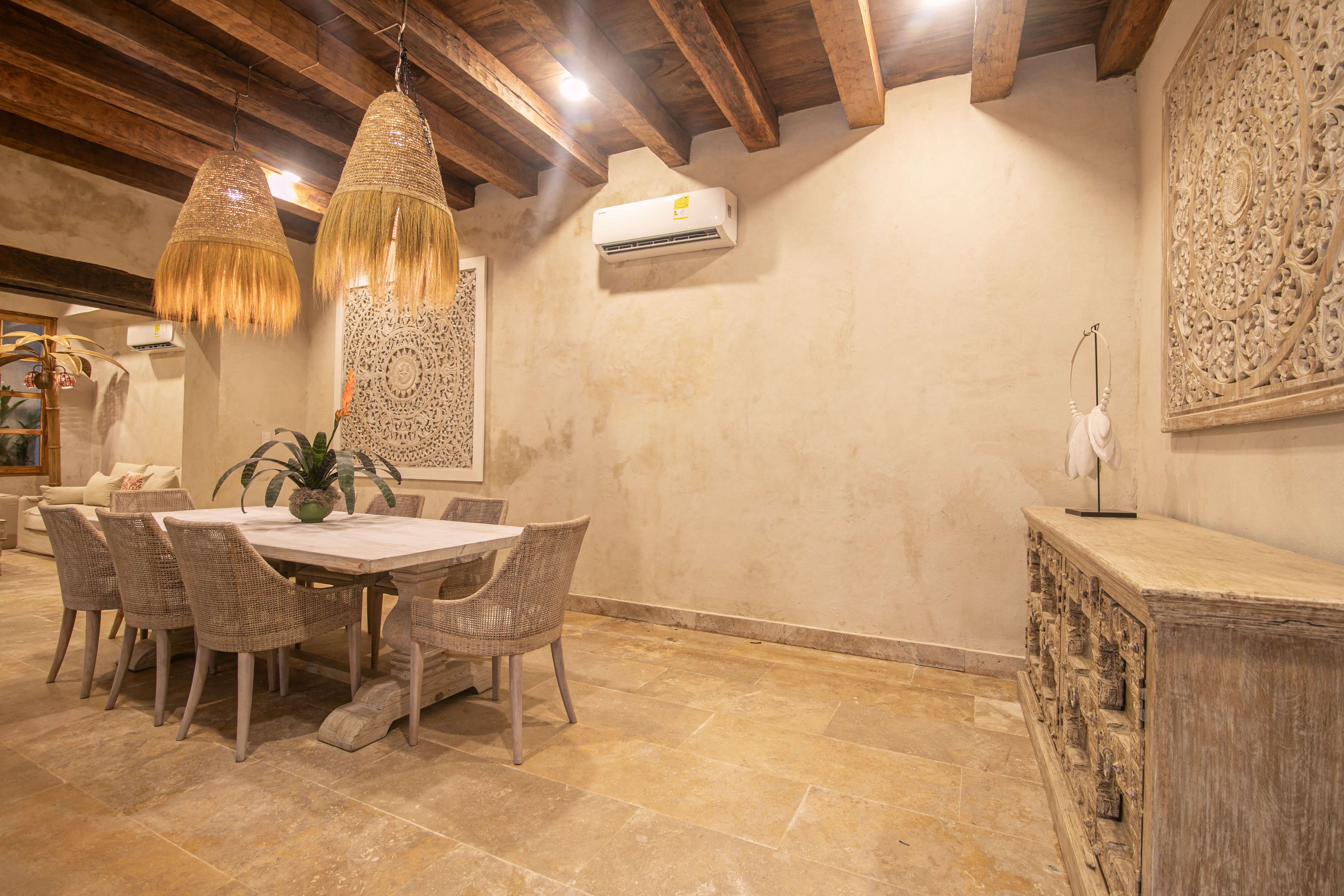A dining area with a round table, wicker chairs, hanging wicker lamps, and a decorative wall panel.