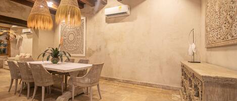A dining area with a round table, wicker chairs, hanging wicker lamps, and a decorative wall panel.