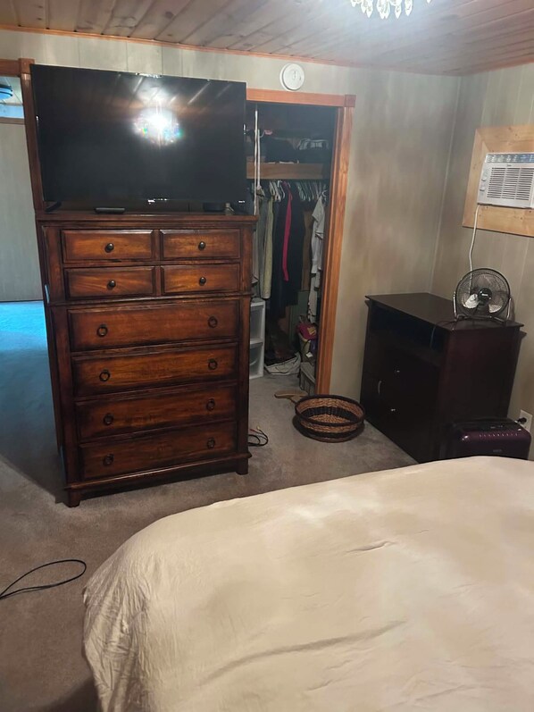 A bedroom with a bed, a wooden dresser, a television, and a fan.