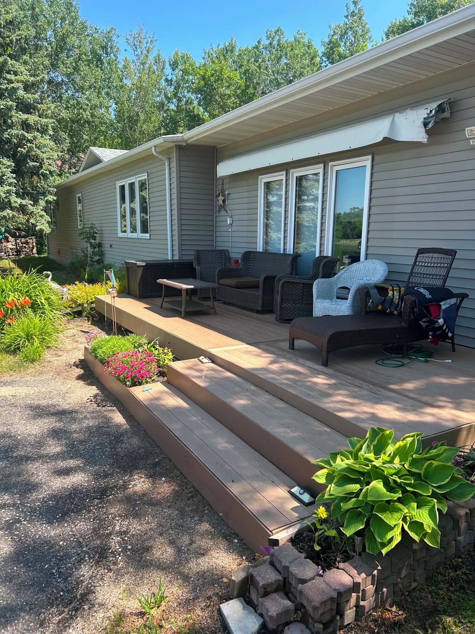 Une maison de plain-pied dotée d’un patio couvert, de mobilier d’extérieur et d’un jardin où poussent différentes espèces de plantes.