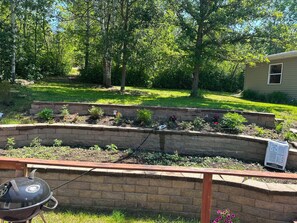 Ein Garten mit Hochbeeten, einem Grill und einem Haus im Hintergrund.