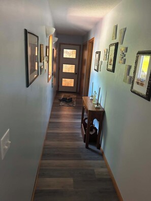A hallway with wooden flooring, a door with frosted glass panels, and wall-mounted picture frames. - Adorable 4-bedroom cabin on charming Lake Metigoshe perfect for relaxing stays. (Bottineau)