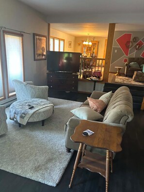 A living room with a sofa, ottoman, and a television. - Adorable 4-bedroom cabin on charming Lake Metigoshe perfect for relaxing stays. (Bottineau)