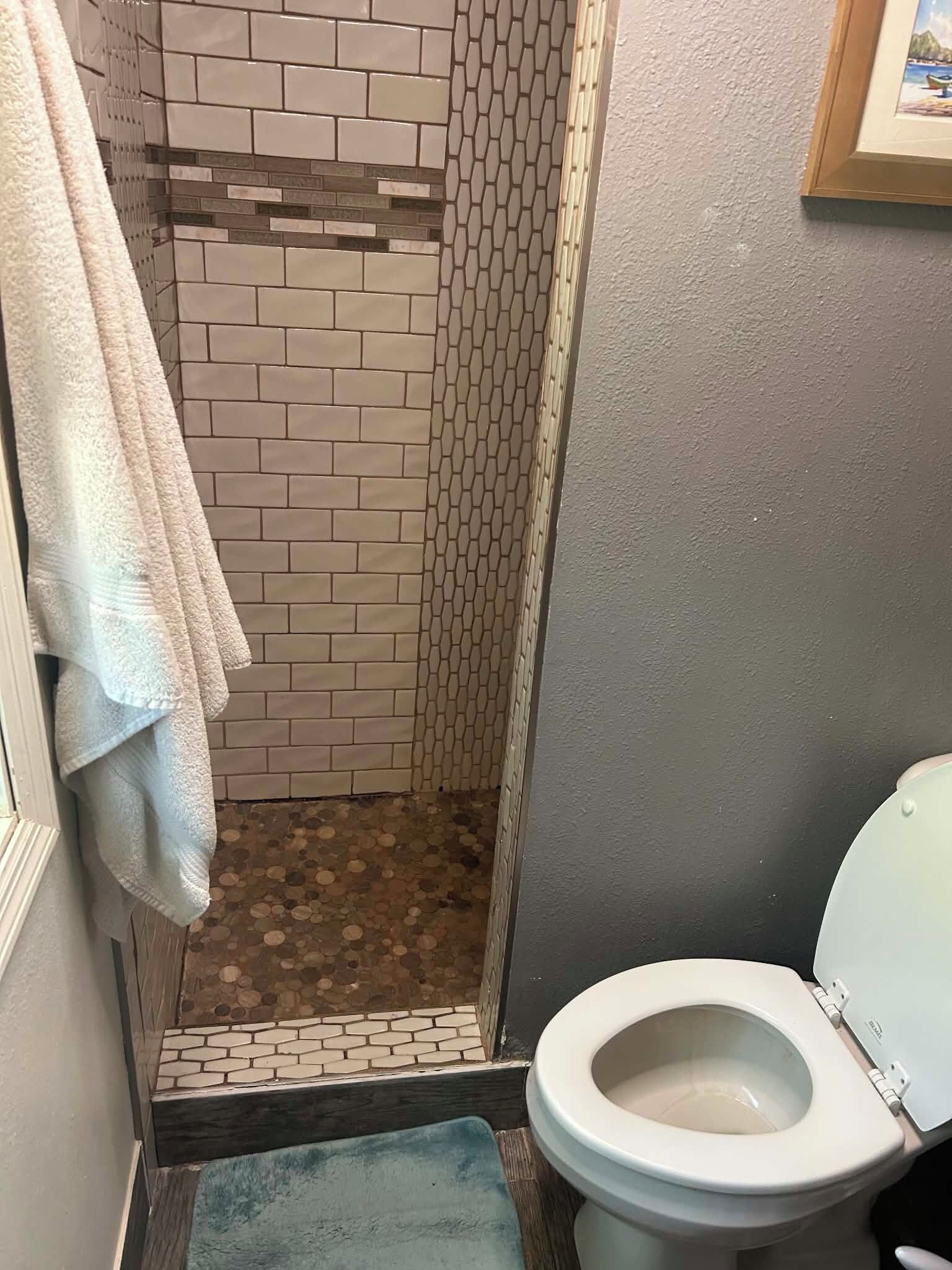 Ein Badezimmer mit Dusche, Toilette und Fliesenboden.
