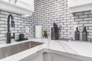 A modern kitchen with a white brick backsplash, a sink with a faucet, and a marble countertop. - LUXE By Marvalous
Luxury 2 bedroom 2 bathroom basement apartment in Brampton. (Brampton)