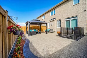 A covered patio area with outdoor furniture, a hanging flower basket, and a gravel pathway leading to a building with a brick facade. - LUXE By Marvalous
Luxury 2 bedroom 2 bathroom basement apartment in Brampton. (Brampton)