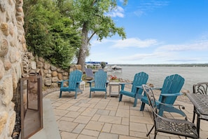 Eine Terrasse mit Adirondack-Stühlen, einem Tisch und Blick auf einen See mit Booten.