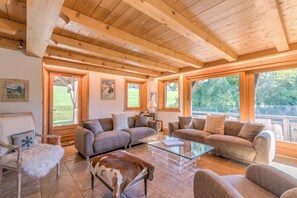 A cozy living room with wooden beams, two sofas, a glass coffee table, and a fur rug. - Chalet Nejma - Welkeys (Megève)