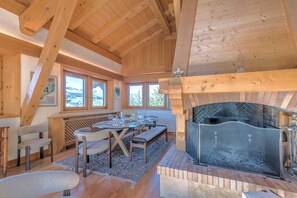 A cozy room with a fireplace, wooden beams, a dining table set for four, and a bench. - Chalet Nejma - Welkeys (Megève)