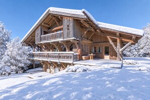 A wooden chalet with a balcony, surrounded by snow-covered trees. - Chalet Nejma - Welkeys (Megève)