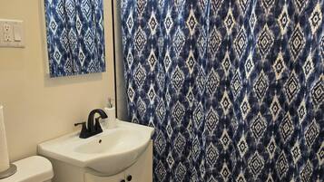 Ein Badezimmer mit einem weißen Waschbecken, einer Toilette und einer Duschvorhang mit geometrischem Muster.