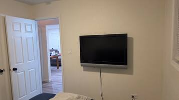 A room with a bed, a television mounted on the wall, and a door leading to another room.