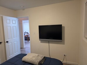 Una habitació amb un llit, una televisió penjada a la paret i una porta que dona a una altra habitació.