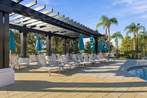 A poolside area with lounge chairs and umbrellas, a pool, and palm trees in the background. - Vista Cay 3BR, Beautiful Lake View, Top Location (Orlando)