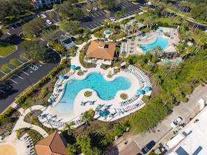 Ett flygbildsfoto av ett semesterområde med en stor pool i mitten, flera mindre pooler och en parkeringsplats.