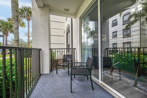 A balcony with a glass door, a chair, and a table. - Vista Cay 2BR, Perfect for Parks and Conventions (Orlando)